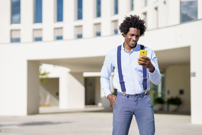 Full length of young man holding smart phone while standing outdoors