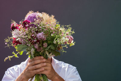 Man covering face with flowers against gray background
