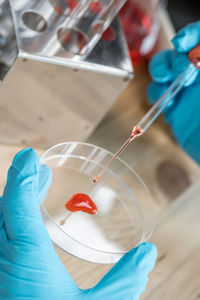 Cropped hands of scientist dropping medical sample from pipette in container