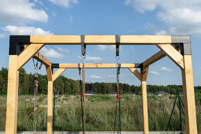 A modern cubic playground made of wooden logs and metal corners, visible nylon ropes and clip hook.