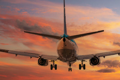 Low angle view of airplane flying against orange sky