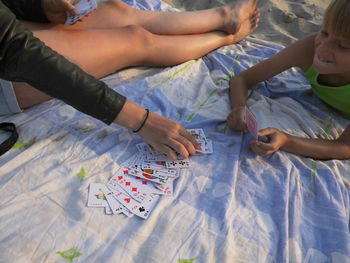 Low section of sister playing cards with brother on blanket at beach