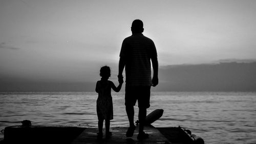 Rear view of silhouette men with daughter standing on pier over sea against sky