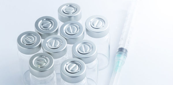 A group of glass vaccine vials sitting next to a hypodermic needle