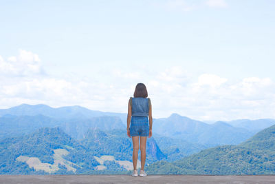 Rear view of woman standing against mountain and sky