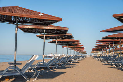 Empty deck chairs and sunshades arranged in a row on sandy beach