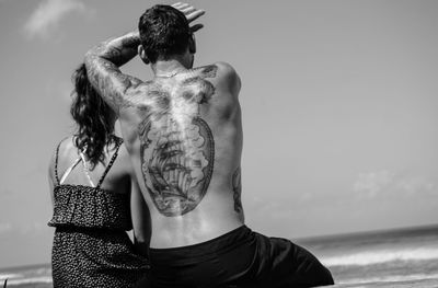 Rear view of shirtless man at beach against sky