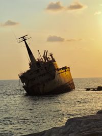 Damaged boat in sea against sky during sunset