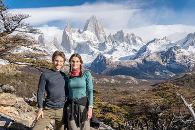 Portrait of friends standing on rock against snowcapped mountains