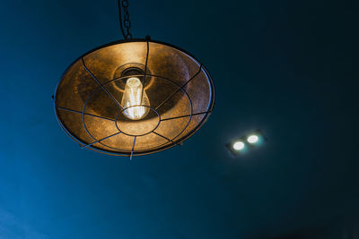 Low angle view of illuminated light bulb against blue sky