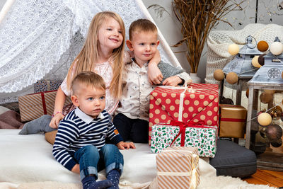 Happy children sit between christmas gift boxes and toys in a decorated house, happy childhood