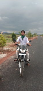 Portrait of man riding motorcycle on road against sky