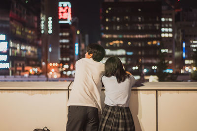 Rear view of couple walking on city street at night