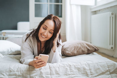 Young woman using mobile phone while lying on bed at home