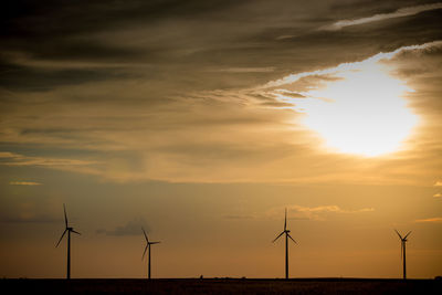 Silhouette wind turbines on landscape against sky during sunset