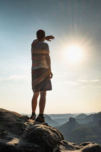 Rear view of man standing on rock against sky