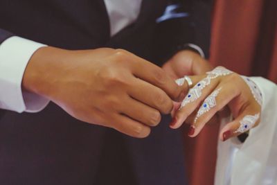 Midsection of bride and groom exchanging rings during wedding