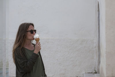 Portrait of a young woman drinking glass against wall