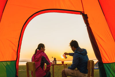 Rear view of people sitting on tent against sky during sunset