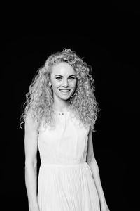 Portrait of smiling woman with curly hair standing against black background