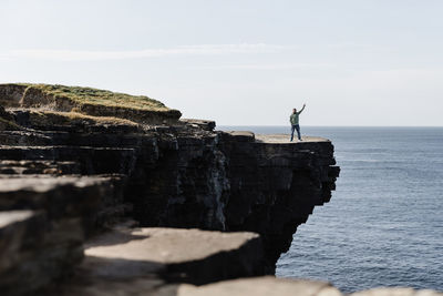 Man standing on cliff by sea against sky