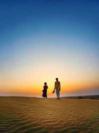 Portrait of people walking on sand against sky during sunset