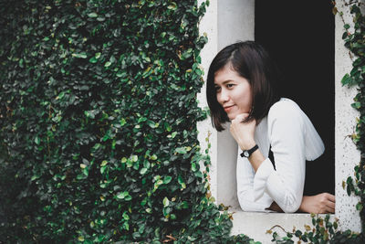 Young woman with hand on chin looking away by plants