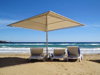 Deck chairs on beach against sky