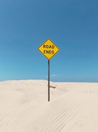 Low angle view of road sign at beach against clear blue sky