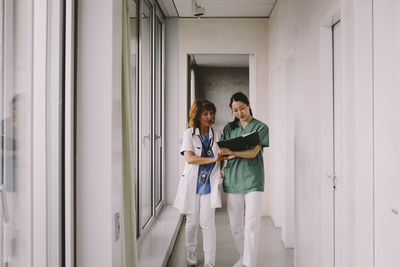 Senior female doctor discussing over record with nurse while walking in hospital corridor