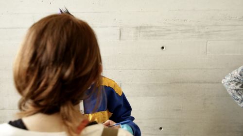 Rear view of woman sitting against wall