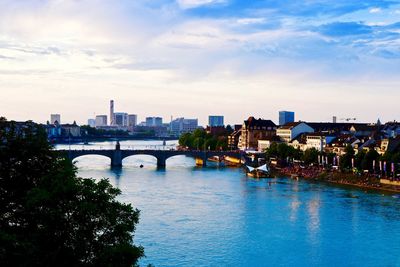 Bridge over river amidst buildings in city against sky