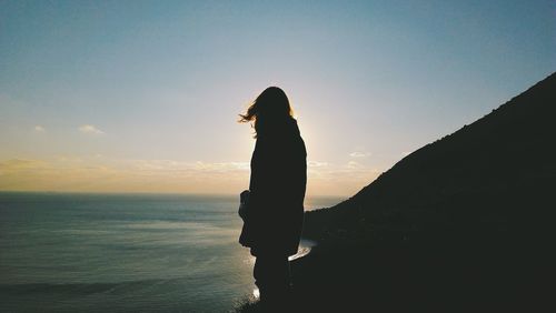 Silhouette person standing on cliff by sea against sky