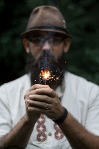 Portrait of young man burning sparkler while standing in forest