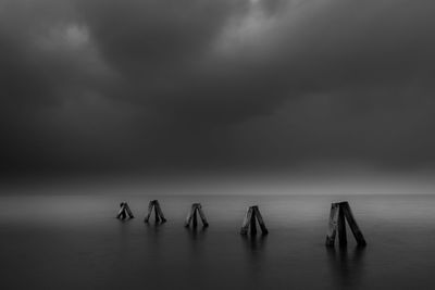 Wooden posts amidst sea against cloudy sky