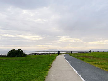 Empty road amidst field against sky