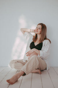 Smiling pregnant woman sitting against wall