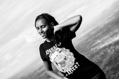 Portrait of smiling young adult standing against cloudy sky