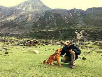 Man looking at dog on field against mountains