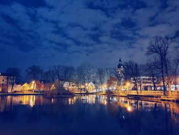 Illuminated buildings by lake against sky at night