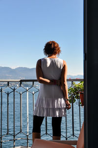 Rear view of young woman standing against lake maggiore on sunny day