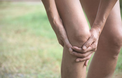 Close-up of person holding knee while standing on land