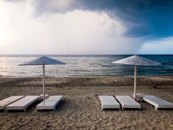 A beach with empty wooden sunbeds and wooden umbrellas on a day with dark storm clouds