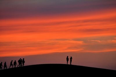 Silhouette people standing against orange sky