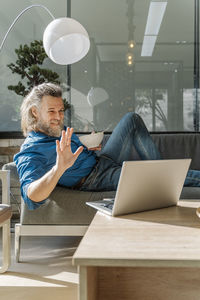 Mature man with a beard eating a salad and looking at his laptop on a