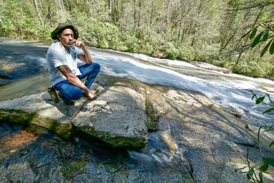 Full length of male hiker sitting on rock in river