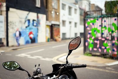 Wing mirror on motorbike showing a brick wall with graffiti in distance 