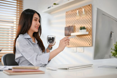 Young woman using mobile phone while working at table