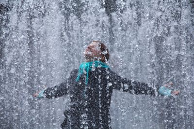 Woman with arms outstretched standing splashing water at fountain