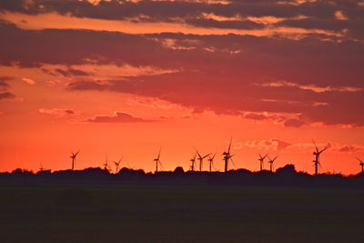 Silhouette wind turbines on field against sky during sunset